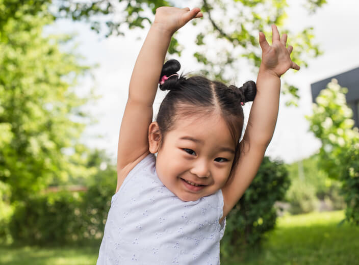 Asian girl toddler Asian girl toddler smiles and lifts her arms above her head.