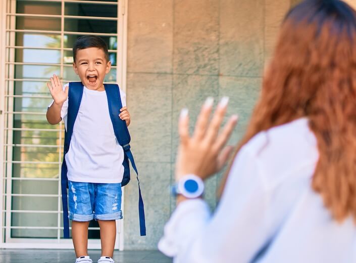 Preschool boy Preschool-aged boy of Latinx descent waves goodbye to his mom on the steps on a school.