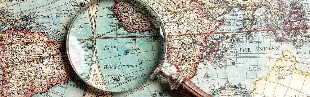 Magnifying glass on aged-looking print map of world.