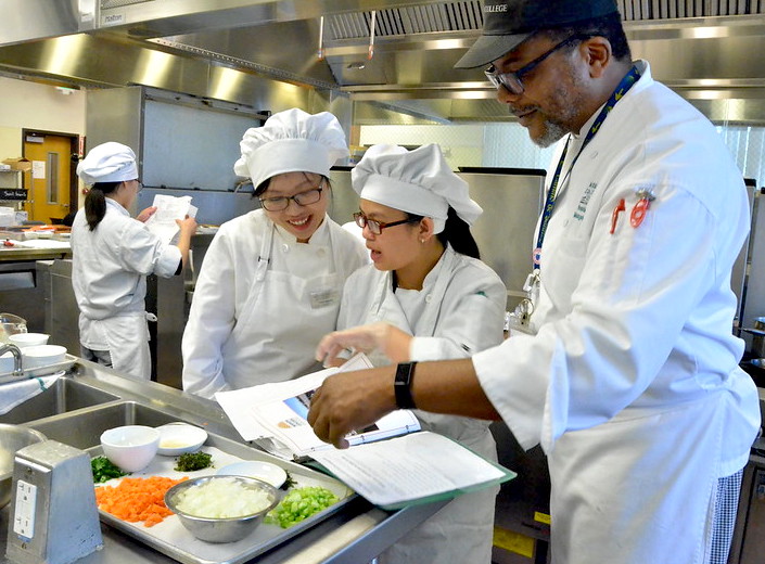 Young woman with white chef's clothes prepares food in industrial kitchen.