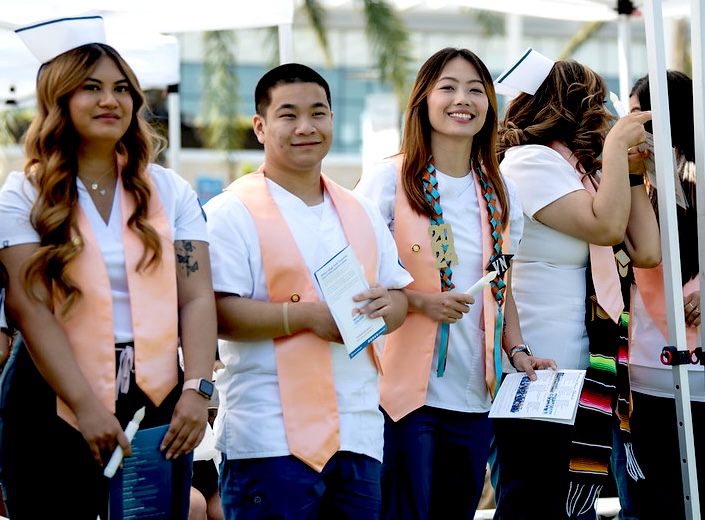 Student nurses. Three student nurses pose in their white scrubs with peach-colored sashes.