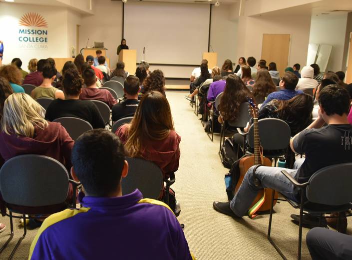 Event People at an event in campus. They sit in chairs facing a screen for a projector.