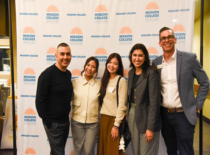Five attendees smiling in front of the Mission College Santa Clara backdrop at the 50th anniversary event.