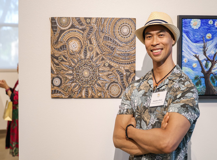 Smiling artist in front of an intricate geometric artwork at the Mission College anniversary gallery.
