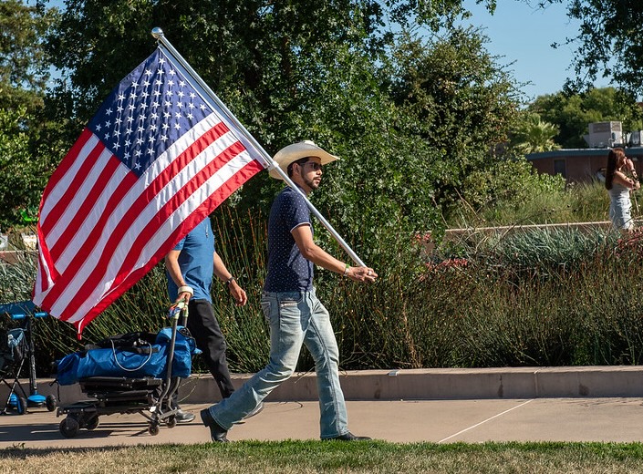 Flag Young Latino man in cowboy hat and jeans carries large American flag.