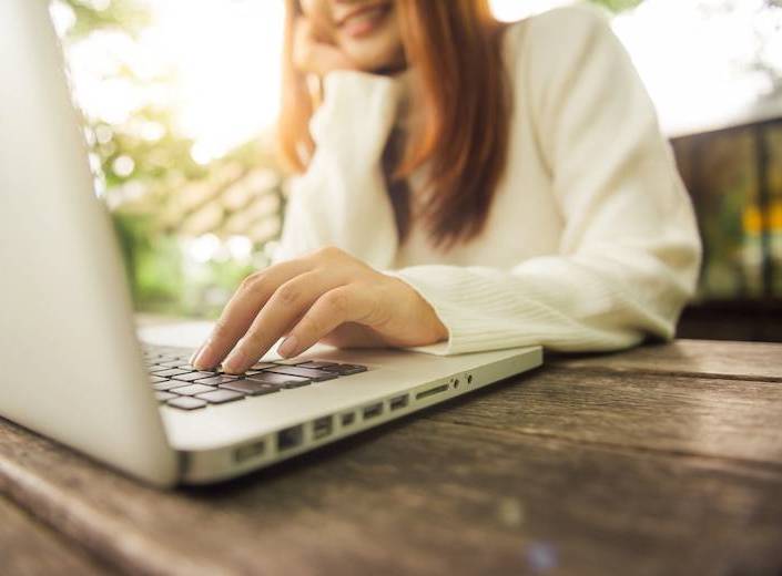 Young woman with light skin and reddish hair works on a laptop.
