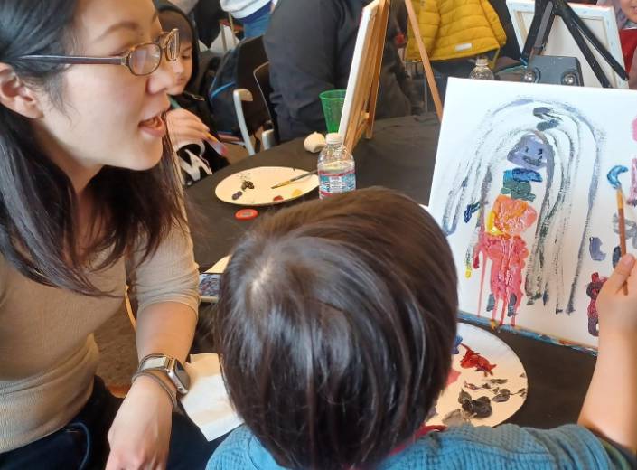 Student Parent Young Asian woman with glasses and straight black hair works with a young boy around four as he works on a painting.