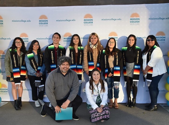 Puente students line up with their sashes at Commencement celebration. Veronica Hand and Javier Huerte kneel in front.
